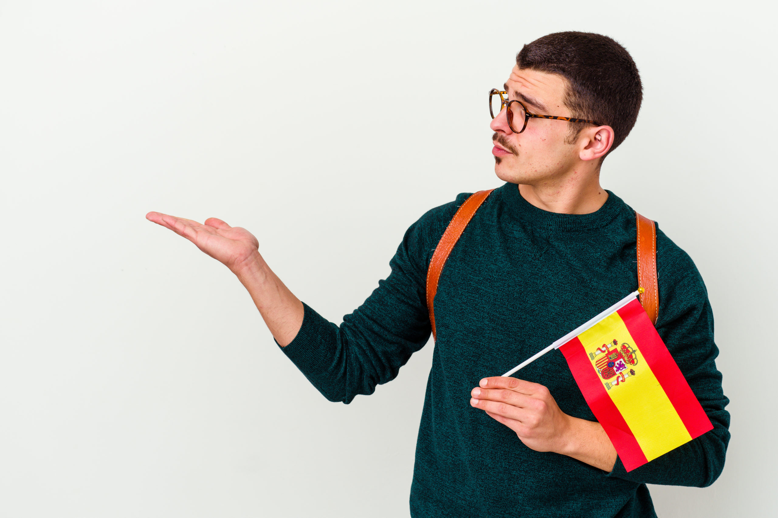 Young caucasian man studying English isolated on white background showing a copy space on a palm and holding another hand on waist.